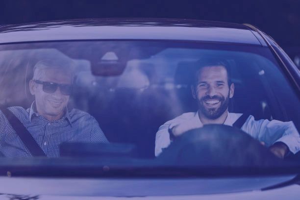 Two men smiling inside a car, one driving and one as passenger.