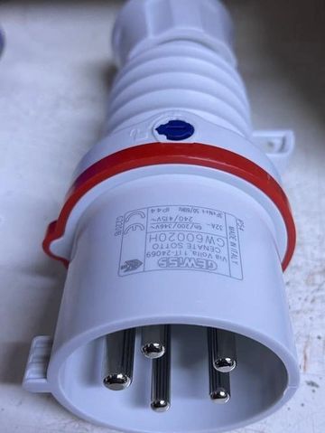 Close-up of a white industrial electrical plug with metal pins and a red ring.