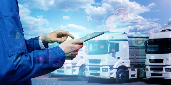 Person using a tablet to manage logistics with trucks in the background.