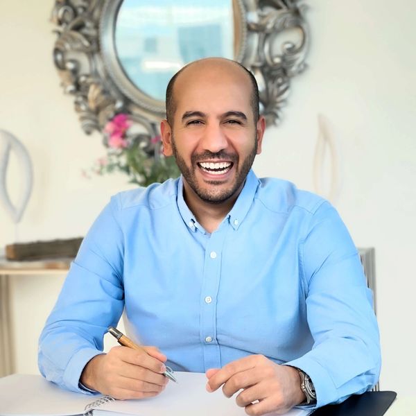 A cheerful man in a blue shirt smiling while writing.