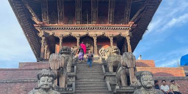Group of tourists posing in front of an ancient multi-tiered temple with stone statues.