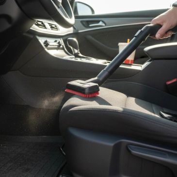 Vacuuming a car seat with a brush attachment.