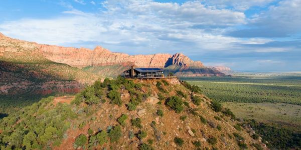 A house perched atop a rocky hill with expansive mountain views under a partly cloudy sky.