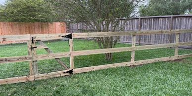 A Corral Board & Wire Fence with a gate surrounding a green yard with trees.
