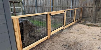 Wood and wire garden gate and fence in a backyard with a tree and wooden fence.