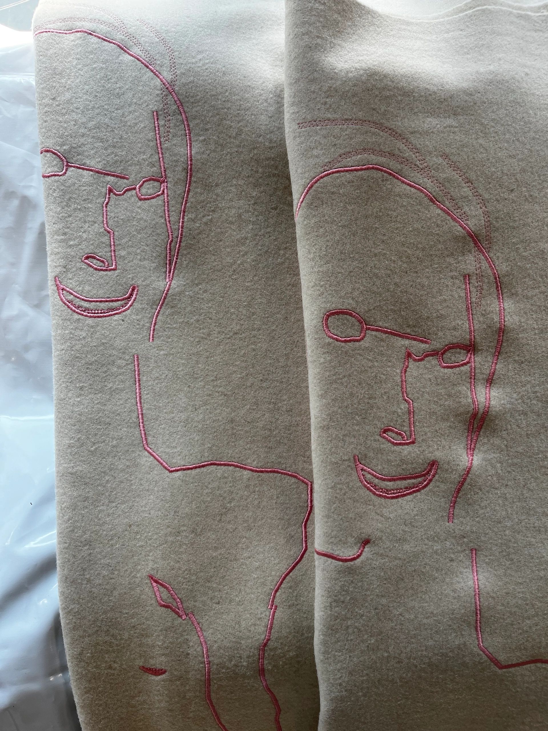 Beige fabric with pink embroidered abstract faces.