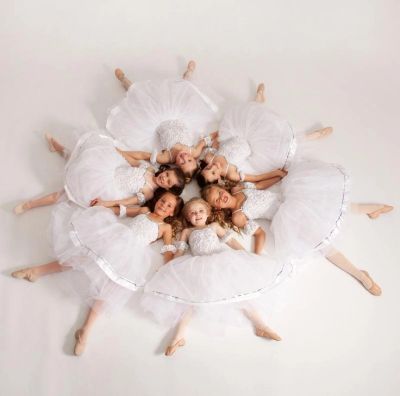 Young ballerinas in white tutus form a circle on the floor.