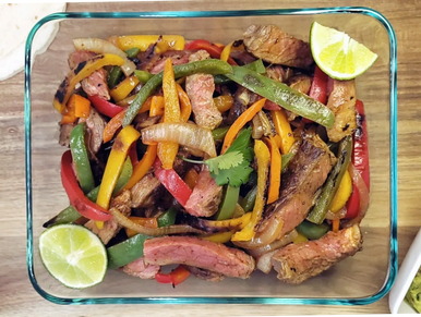 Grilled steak fajitas with bell peppers in glass container with lime wedges