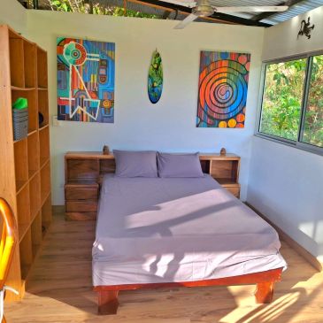 A cozy bedroom with a neatly made bed and colorful abstract paintings on the wall.