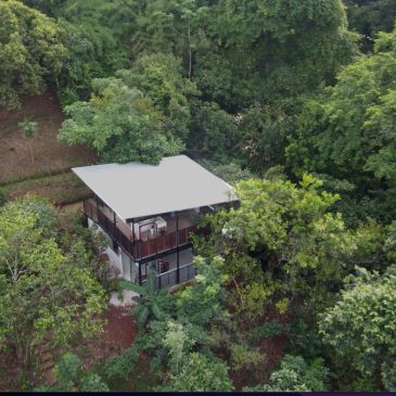 A modern two-story house surrounded by dense green trees.