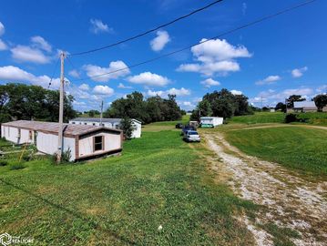 Rural landscape with mobile homes, cars, and a dirt path under a blue sky.