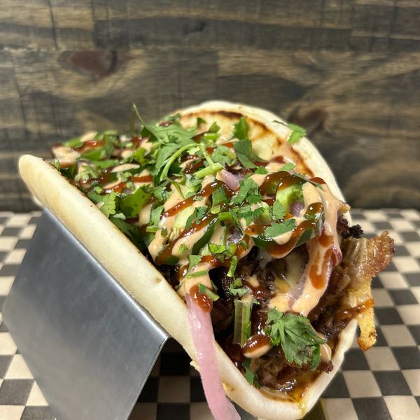 Close-up of a taco with grilled meat, cilantro, sauce, and pickled onions in a soft tortilla.