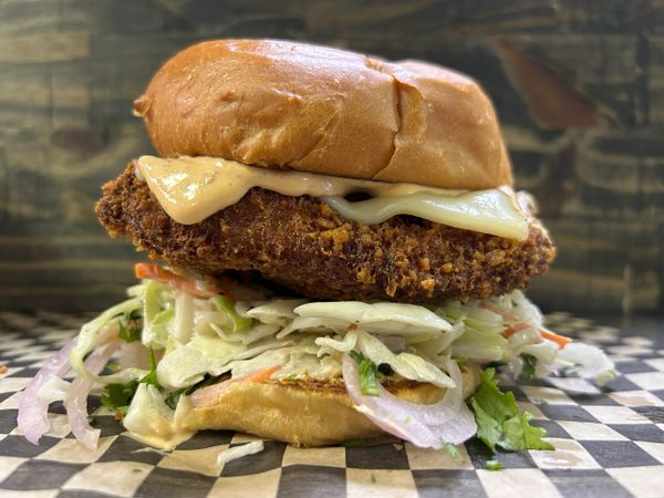 Close-up of a crispy fried chicken sandwich with slaw and sauce.
