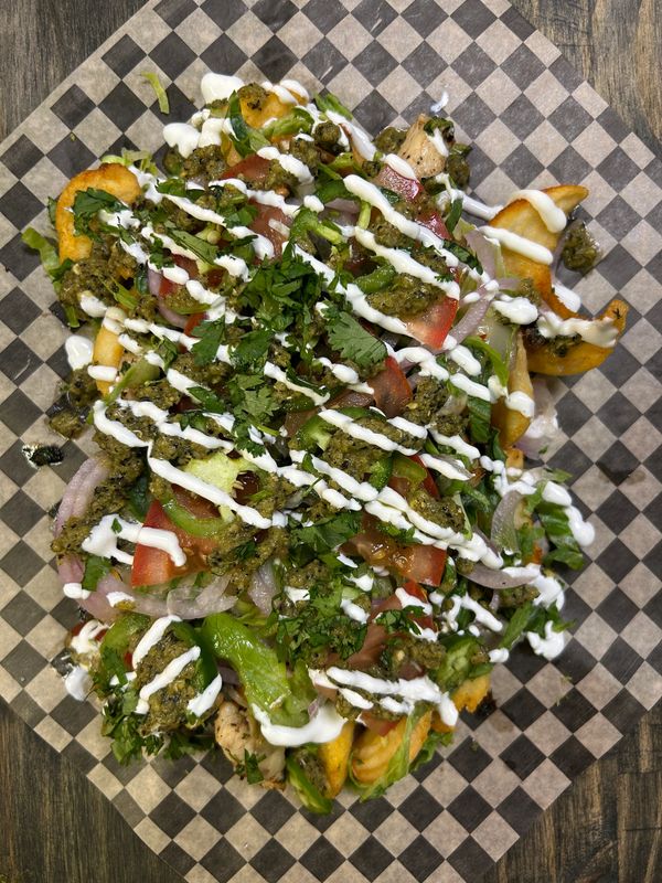 Loaded fries topped with greens, tomatoes, onions, sauce, and herbs.