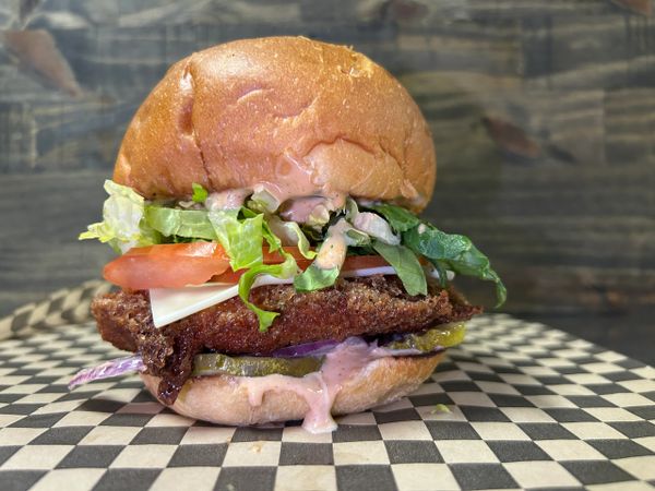 Crispy chicken sandwich with lettuce, tomato, cheese, pickles, and sauce on a bun.