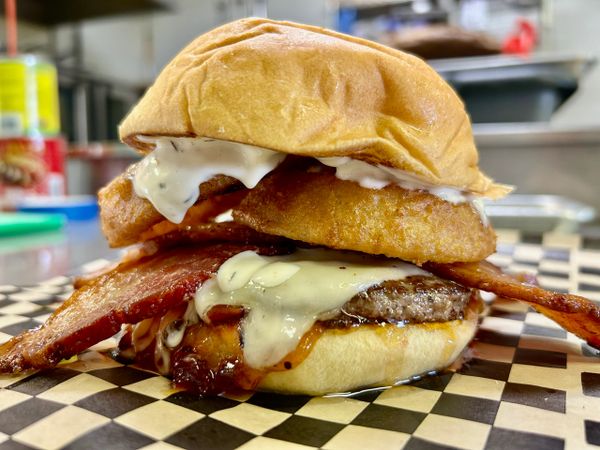 Close-up of a loaded bacon cheeseburger with fried onion rings and creamy sauce.