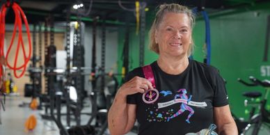 Older woman proudly holding a medal and paddle in a gym.