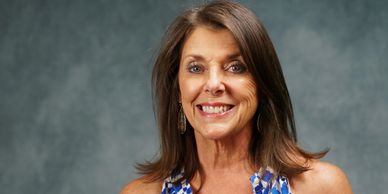 Smiling woman in a blue and white patterned dress against a gray backdrop.