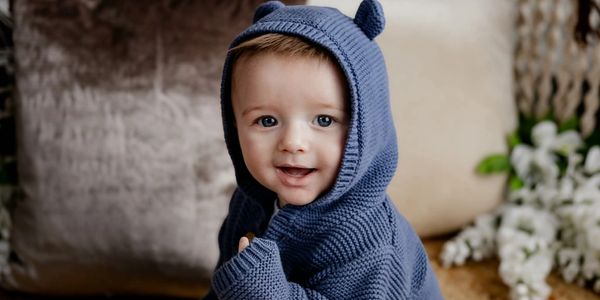 Smiling baby in a blue knit hoodie with bear ears.