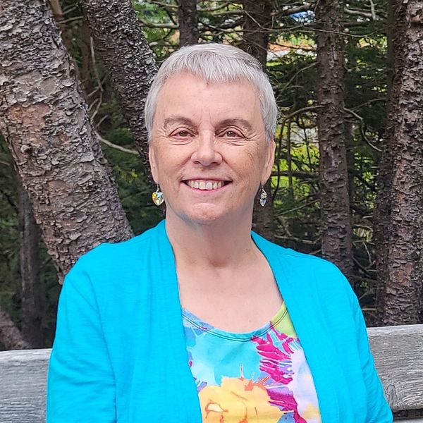 Smiling elderly woman in a bright blue cardigan, sitting outdoors.