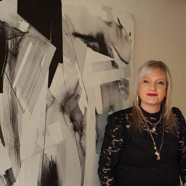 Woman in black lace dress stands beside abstract black and white painting.