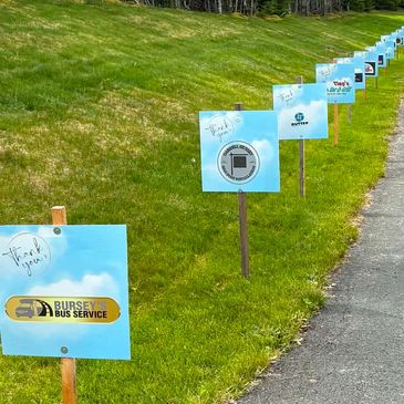 Row of blue signs thanking various service providers on grass.