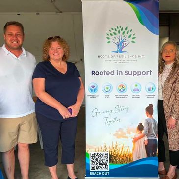 Group of three people standing by a banner for Roots of Resilience Inc.