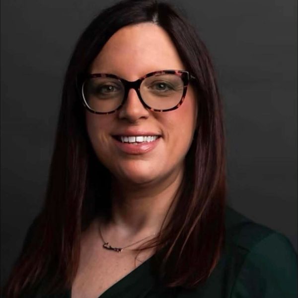 Smiling woman with glasses and dark hair against a black background.
