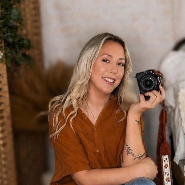 Smiling woman holding a camera, wearing a rust-colored top.