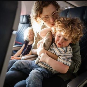 A mother comforts her crying child on an airplane seat.