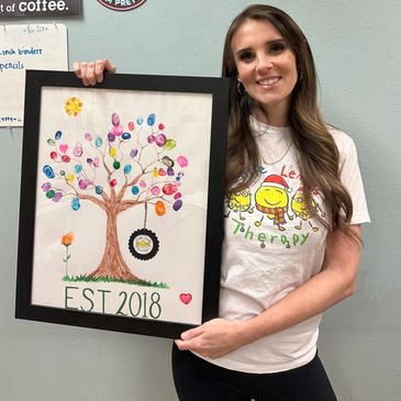 Woman proudly holding framed thumbprint tree art labeled EST 2018.