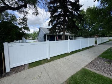 White vinyl fence surrounding a house with trees.