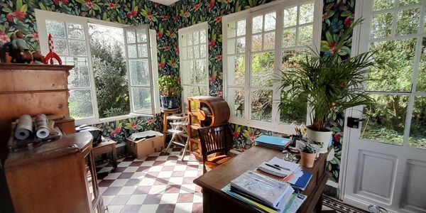 Sunlit room with floral wallpaper and wooden furniture overlooking a garden.