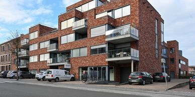 Modern brick apartment building with balconies and parked cars.