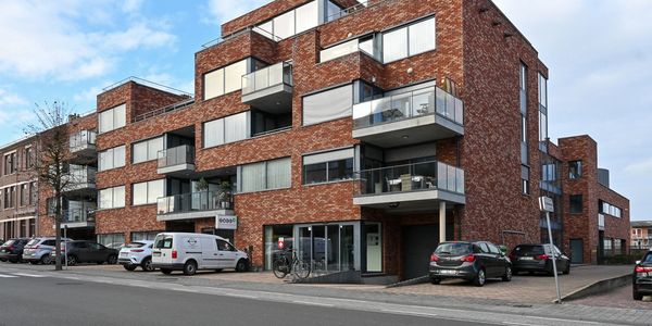 Modern brick apartment building with balconies and parked cars.