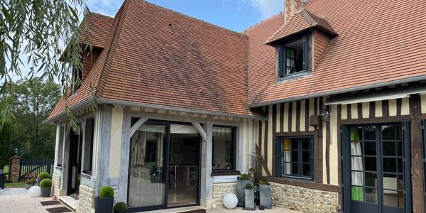 Charming rustic house with a tiled roof and large windows surrounded by plants.