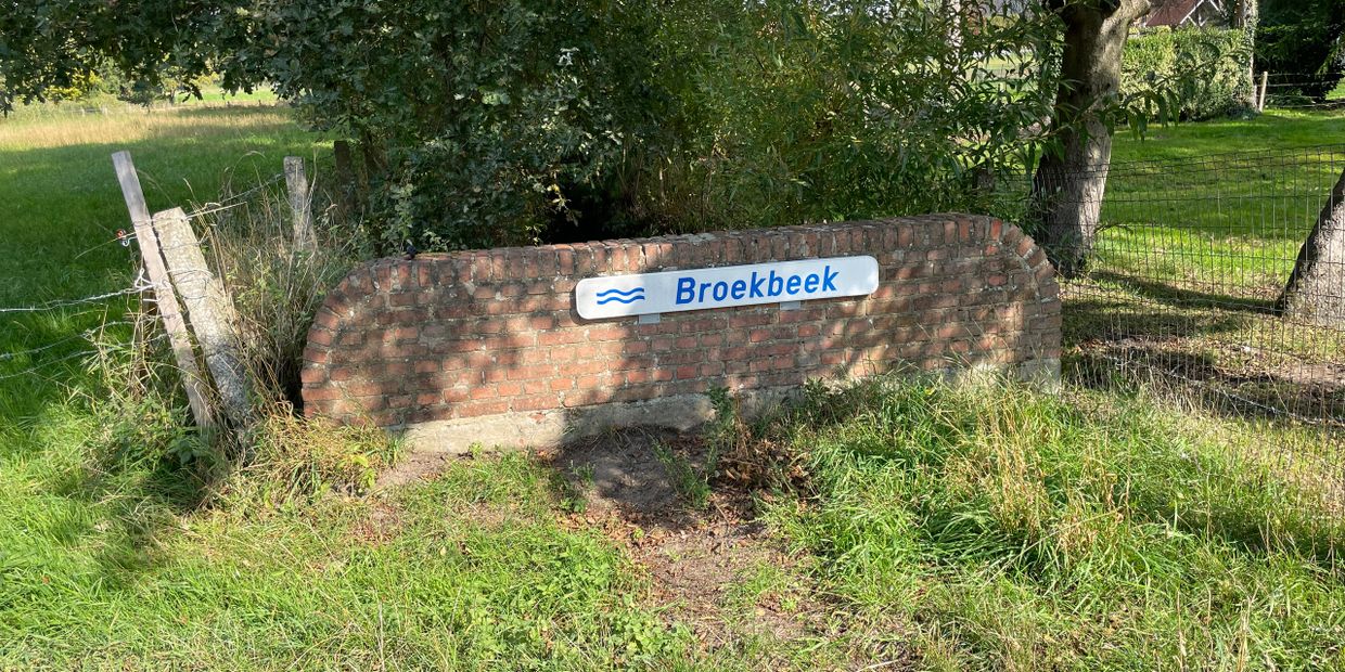 A brick sign with the name Broekbeek surrounded by grass and trees.