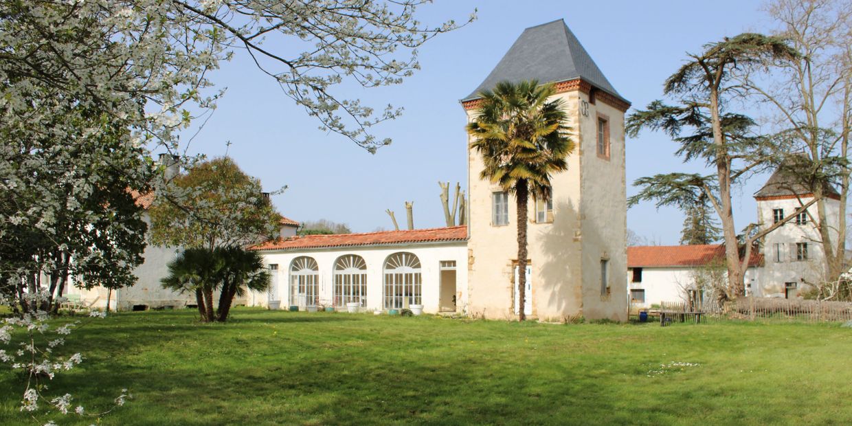 Historic stone buildings with a tall tower surrounded by trees and a green lawn.