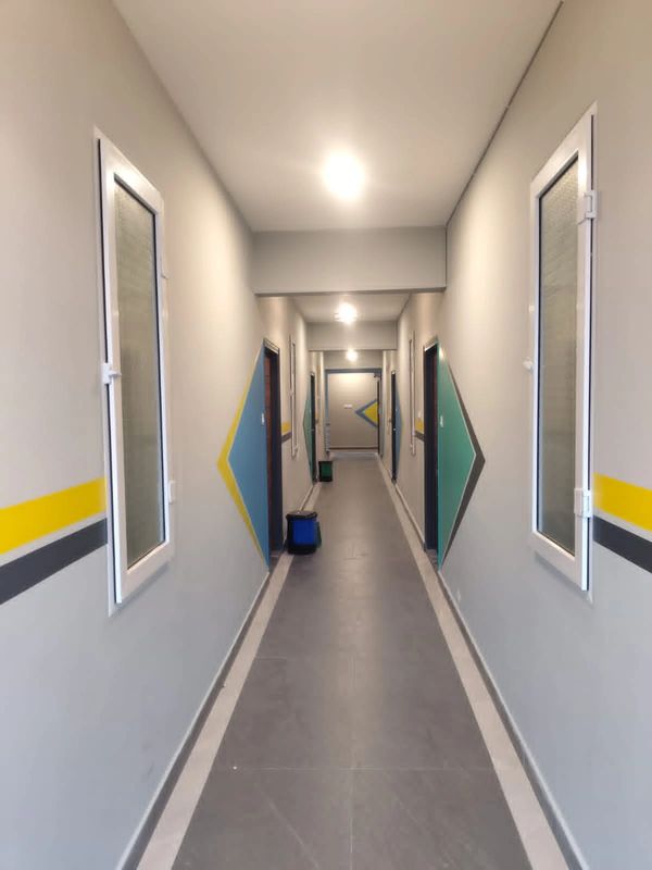 A clean, well-lit hallway with geometric wall designs and windows on both sides.
