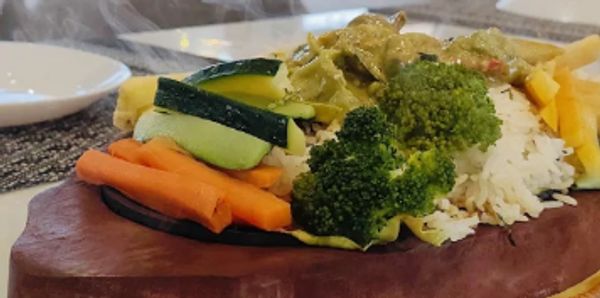 Steaming hot meal with rice, vegetables, and fries on a wooden platter.