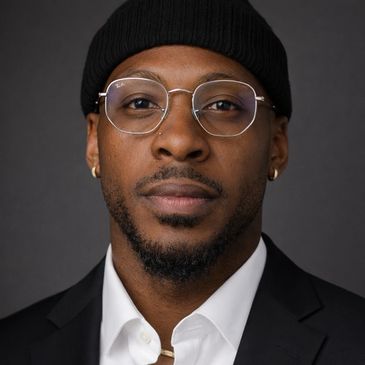 Portrait of a man wearing glasses, a black beanie, and a suit jacket.
