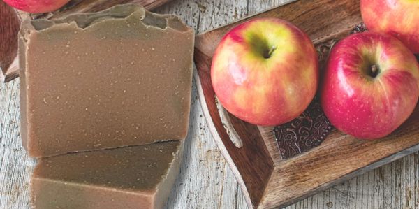 Handmade soap bars next to fresh apples on a wooden table.