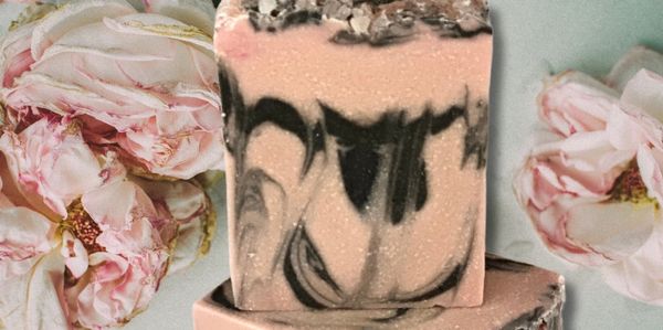Artisan soap with pink and black marbled design beside pink roses.