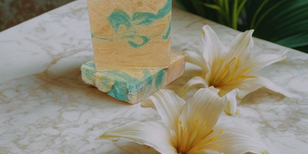 Handcrafted soap bars with blue swirls beside white lilies on marble surface.