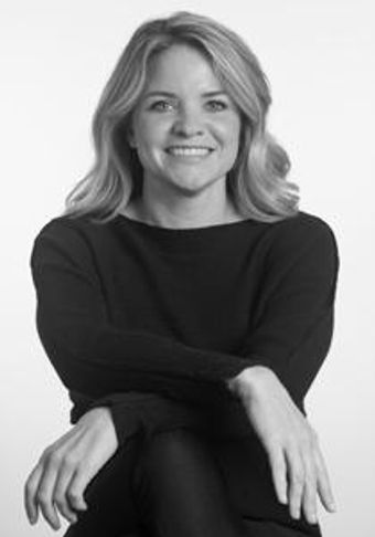 Smiling woman with blonde hair in a black outfit sitting with crossed arms.