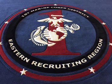 Embroidered emblem of 1st Marine Corps District, Eastern Recruiting Region on a blue carpet.