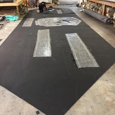 Large black fabric laid out with transparent patterns and a person working on it.