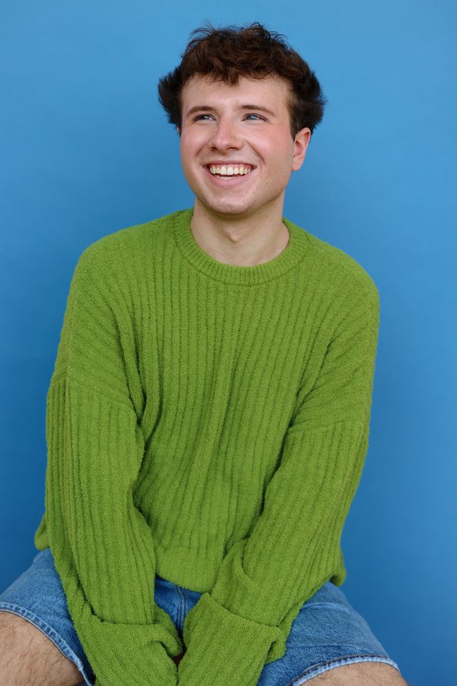 Young man in green sweater smiling against blue background.