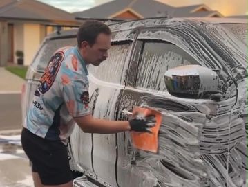 Man washing a car with soap and sponge.