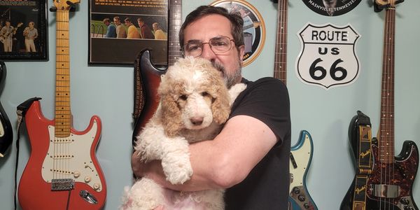 Man holding a fluffy dog in a music-themed room with guitars on the wall.